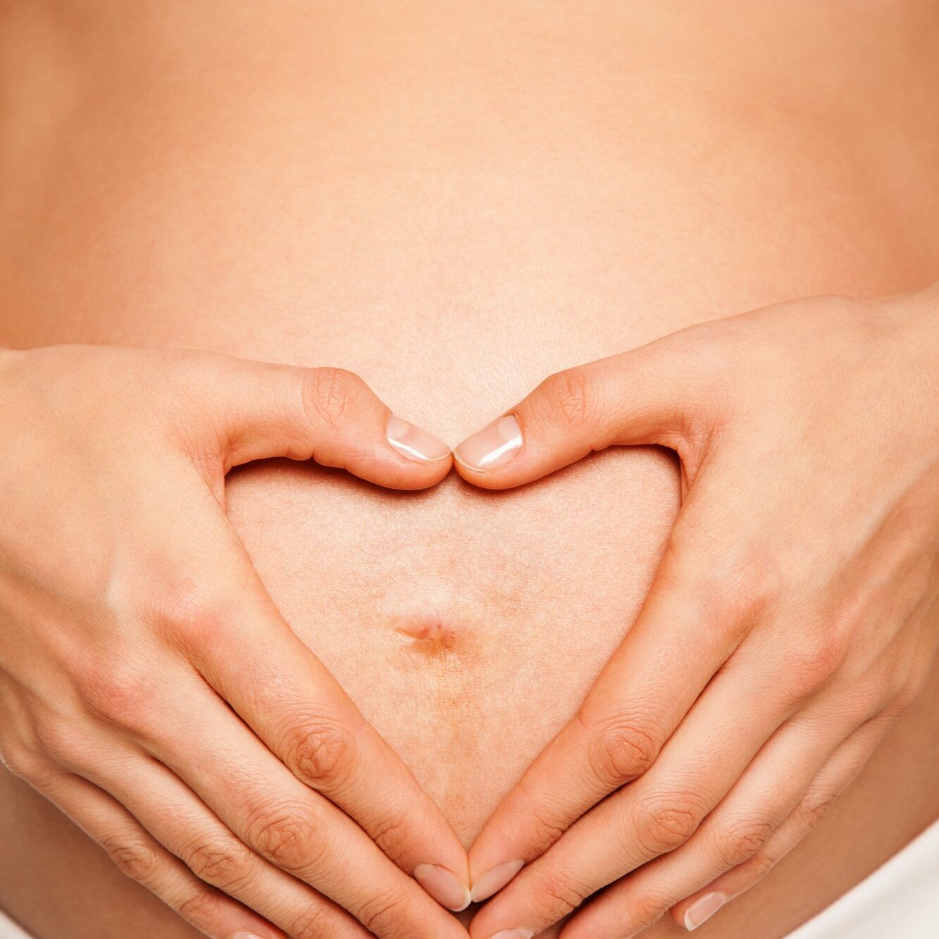 Close-up - hands of a pregnant woman making heart shape in front abdomen, white underwear.